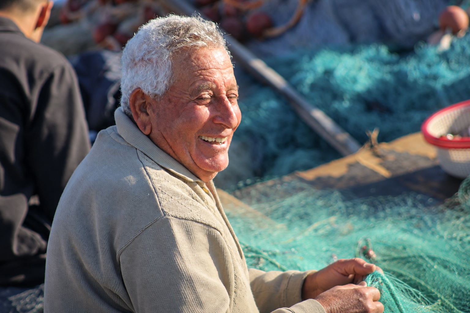 A smiling fisherman mending a green net