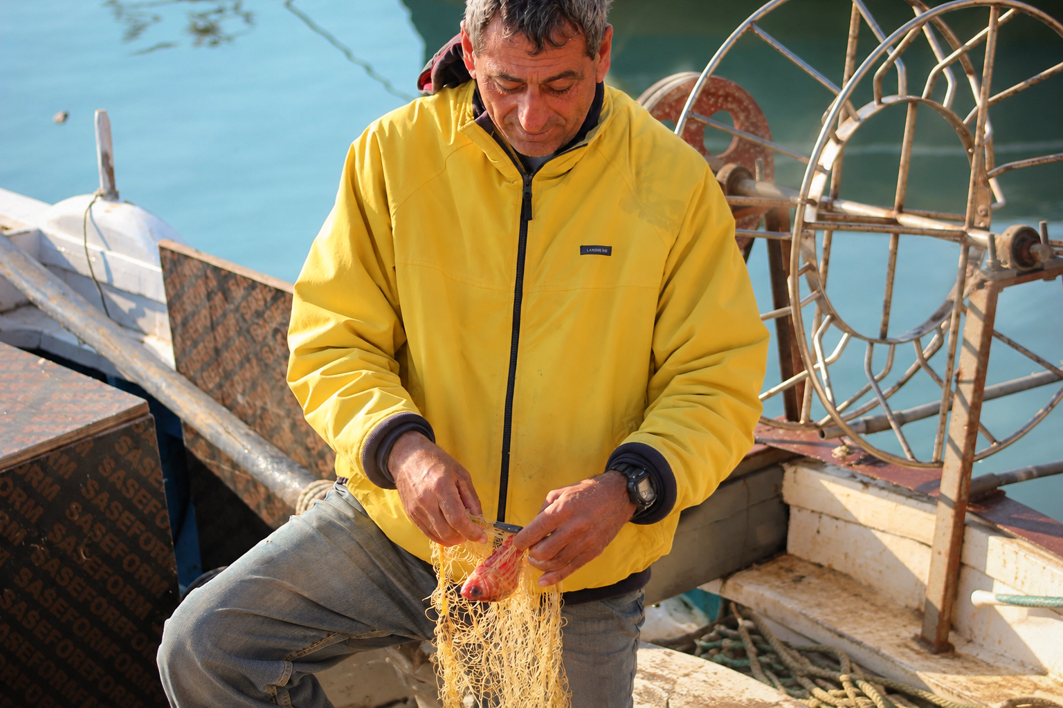 A fisherman in a yellow jacket untangling a net on his boat