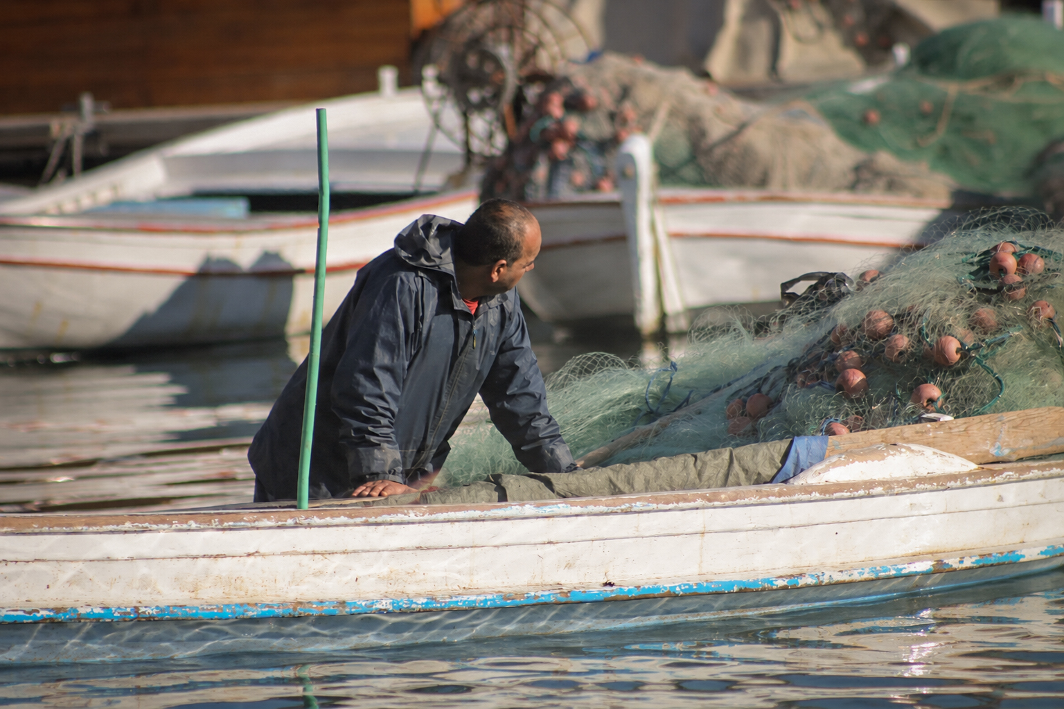 A fisherman standing in his boat, nets piled behind him