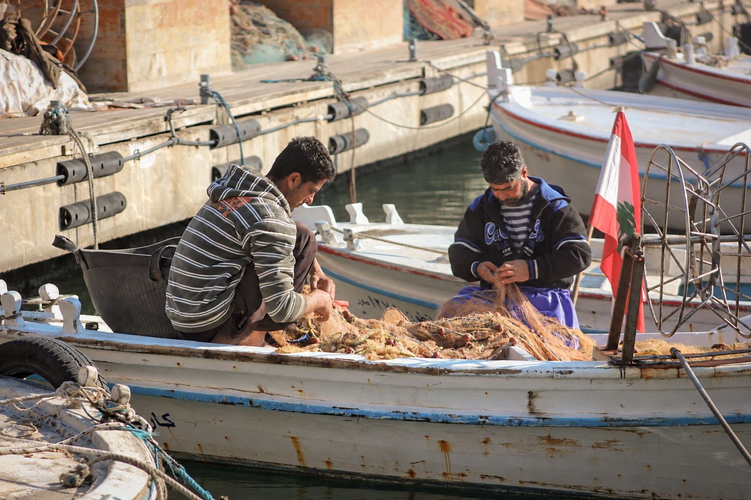 Two fishermen at work in a boat flying the Lebanese flag